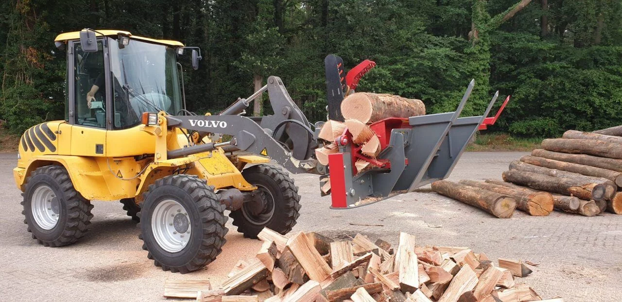 Compacte Volvo shovel met BTD houtklover verwerkt boomstammen tot brandhout op industrieterrein, efficiënte houtverwerking in actie.
