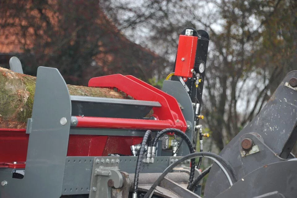 Zijaanzicht van een BTD houtkloofmachine met boomstam in invoerpositie, hydraulische leidingen en bedieningsunit zichtbaar op de achtergrond.
