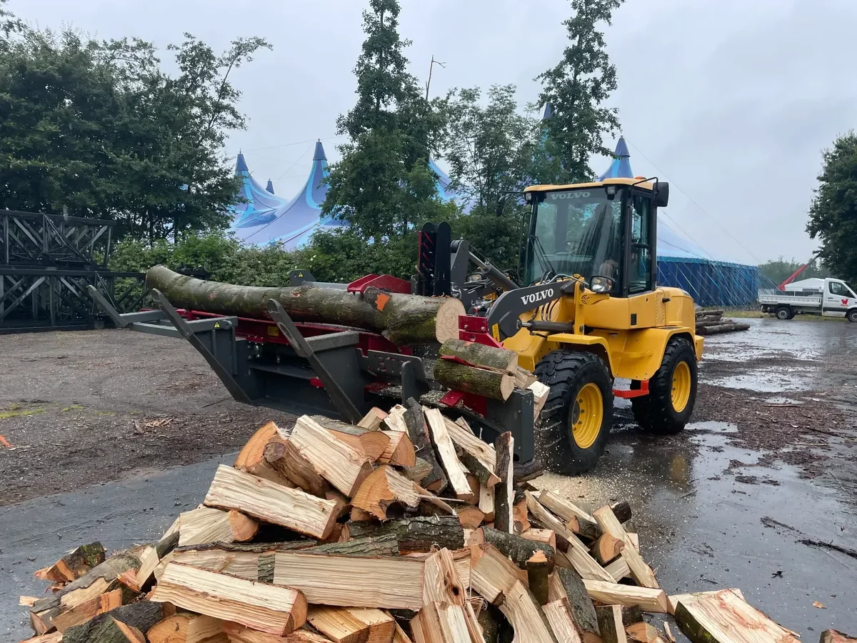Volvo shovel met BTD houtklover aan het verwerken van boomstammen tot gekloofd brandhout op buitenterrein