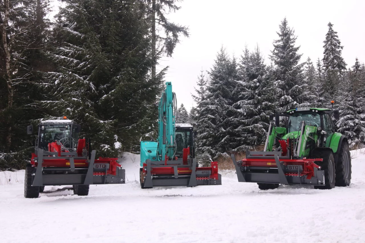 BTD houtkloofmachines gemonteerd op tractor, graafmachine en shovel in besneeuwd bosgebied – winterdemonstratie van houtverwerkingsapparatuur in extreme omstandigheden.