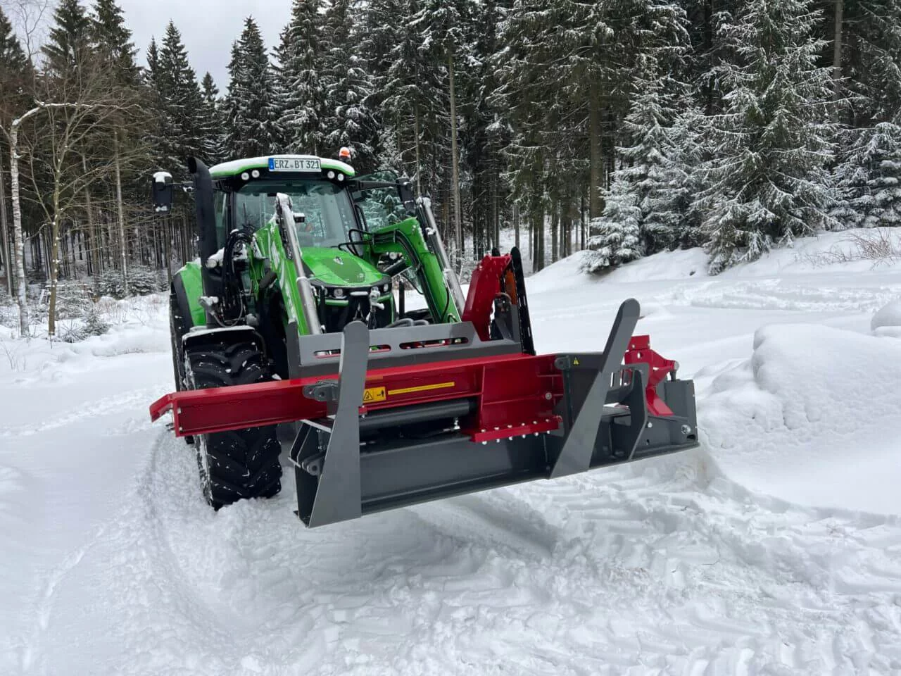 Groene tractor met aangekoppelde BTD houtkloofmachine in besneeuwd bosgebied, klaar voor brandhoutverwerking in winterse omstandigheden.
