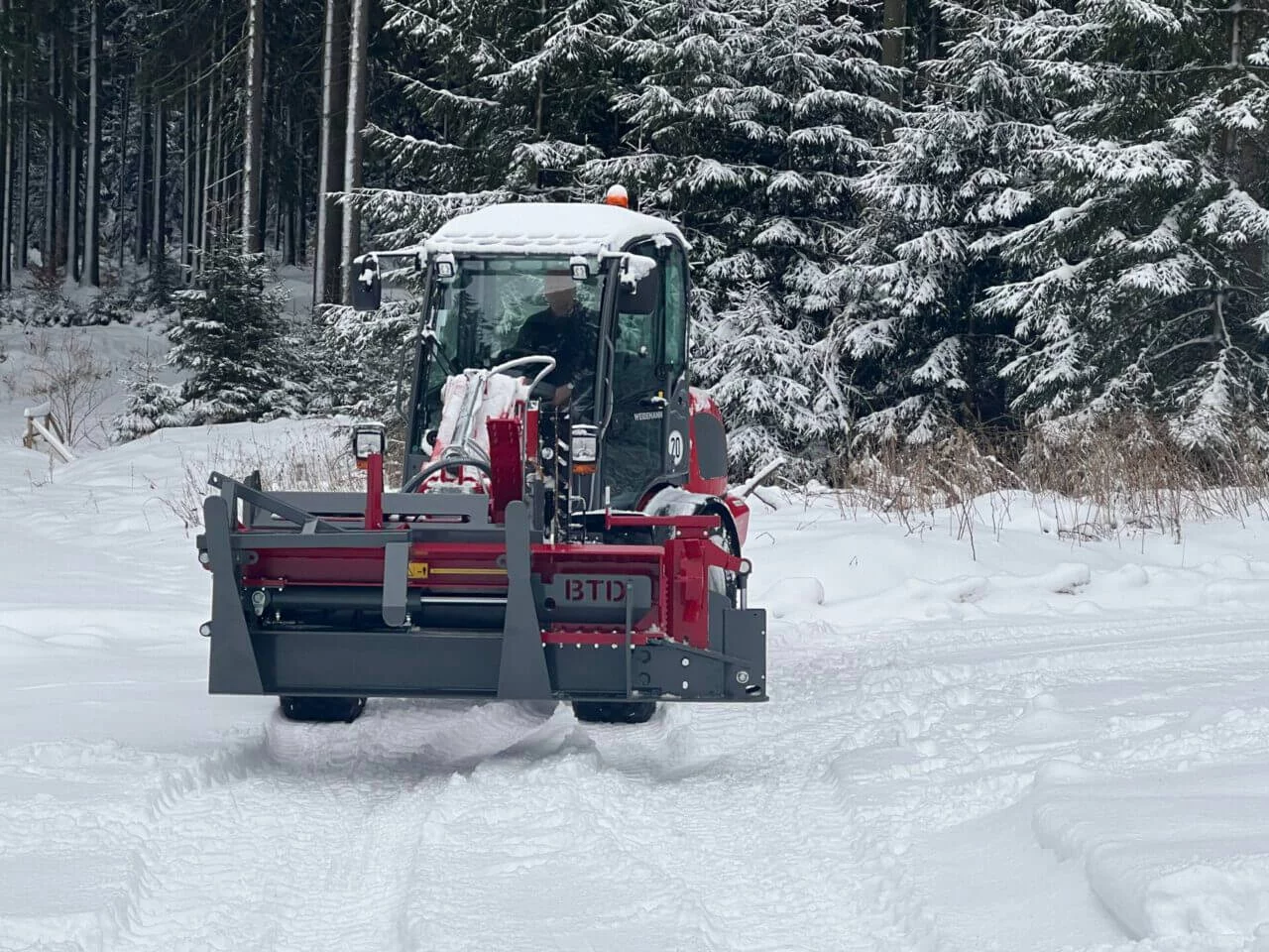Weidemann machine met aangekoppelde BTD houtkloofunit rijdt door besneeuwd bosgebied, klaar voor houtverwerking in winterse omstandigheden.