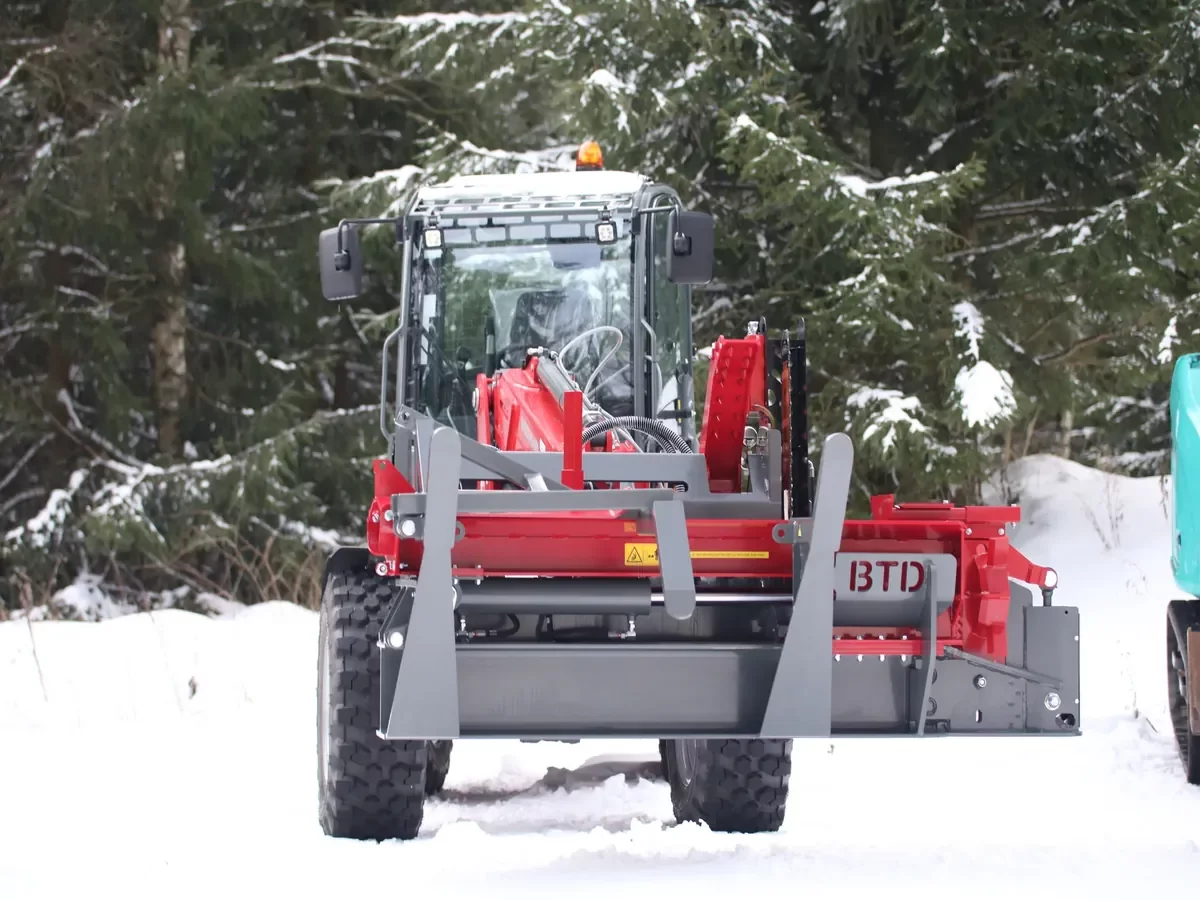 PROplus houtkloofmachine bevestigd aan Weidemann shovel, actief in besneeuwd bosgebied voor professioneel houtbeheer