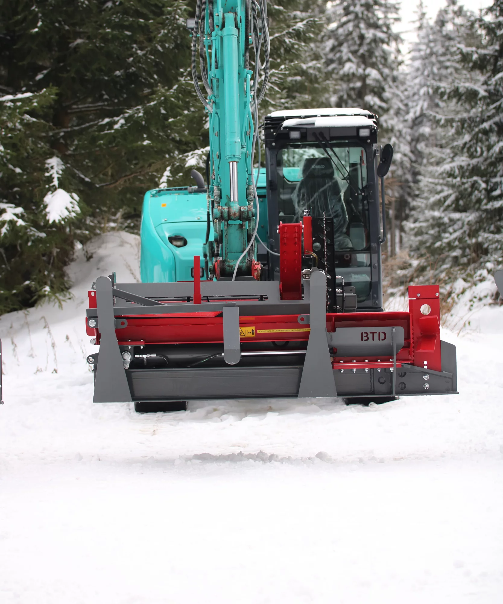 Graafmachine met aangekoppelde rode en grijze sneeuw- of grondschuif van BTD, werkend in een besneeuwd bosgebied.
